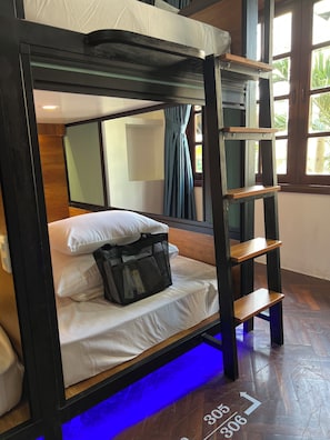 Una cama individual con cabecera, una mesita de noche, una bolsa y una ventana con cortinas.