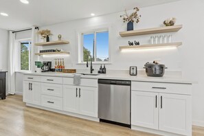 A modern kitchen with white cabinets, a dishwasher, a coffee machine, and a window with a view. - Lavishly Spacious Modern (Seattle)