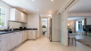 Een moderne keuken met een centraal eiland, een eethoek met een televisie, en een gang naar een woonkamer.