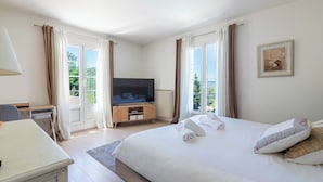Een slaapkamer met een bed, een televisie, een bureau en een raam met gordijnen.