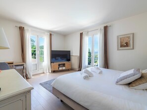 Ein Schlafzimmer mit Bett, Fernseher, Schreibtisch und einem Fenster mit Vorhängen.