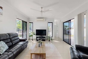 A modern living room with a black leather sofa, a wooden coffee table, a flat-screen TV, and large windows.