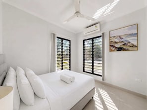 A modern bedroom with a bed, white pillows, a ceiling fan, an air conditioning unit, and a painting on the wall.
