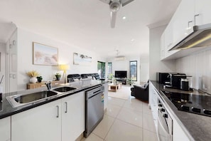 A modern kitchen with a built-in oven, a dining area with a black sofa, and a living room with a TV.
