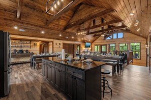 A spacious kitchen with a large island, wooden beams, and a stone fireplace. - Sleeps 30 | Heated Pool | Arcade, Game Room & Theater | Mtn Views (seveirville)