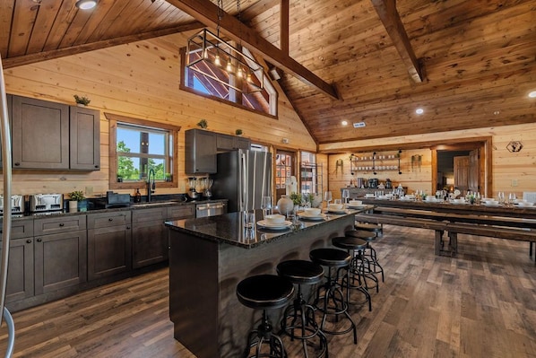 A spacious kitchen with a large island, bar stools, and a long dining table. - Sleeps 30 | Heated Pool | Arcade, Game Room & Theater | Mtn Views (seveirville)