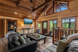 A wooden interior with a dining area, sofas, and a view of the outdoors. - Sleeps 30 | Heated Pool | Arcade, Game Room & Theater | Mtn Views (seveirville)