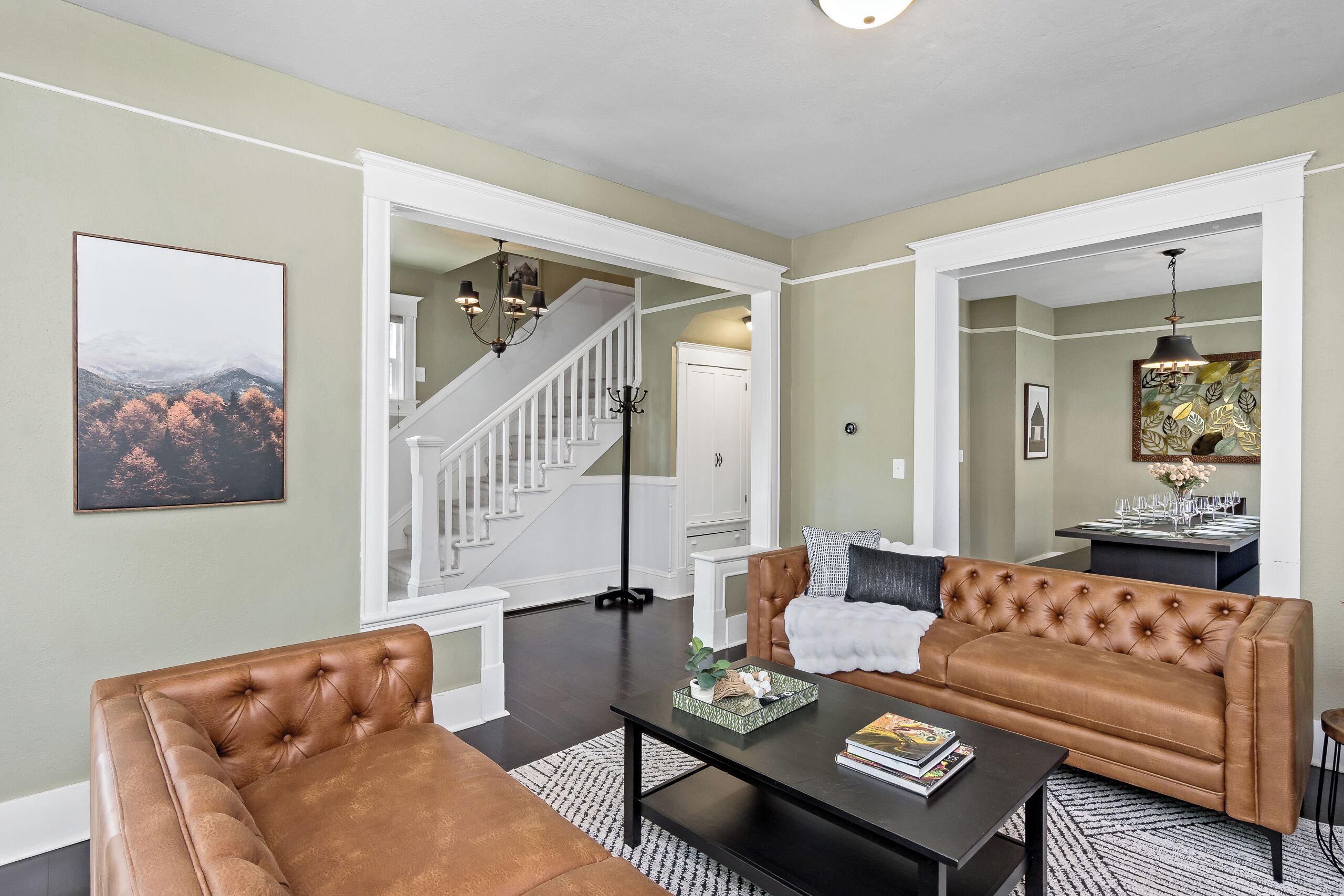 A living room with a brown leather sofa, a black coffee table, and a staircase leading to another room.
