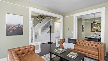 A living room with a brown leather sofa, a black coffee table, and a staircase leading to another room.