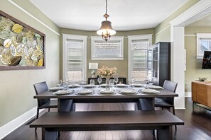 A dining room with a dark wooden table set for six, a chandelier, and a large abstract leaf artwork on the wall.
