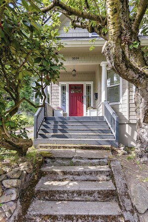 A house with a red door, a front porch, and a staircase leading to the entrance.