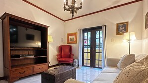 A living room with a television, a red armchair, a sofa, a coffee table, and a chandelier. - The Sanctuary Private Pool & outdoor spa (Rincón)