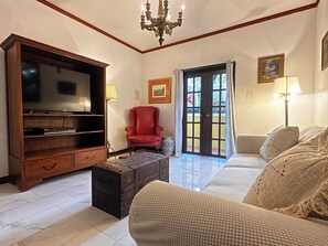 Ein Wohnzimmer mit Fernseher, einem roten Sessel, einer Couch, einem Couchtisch und einer Deckenleuchte.