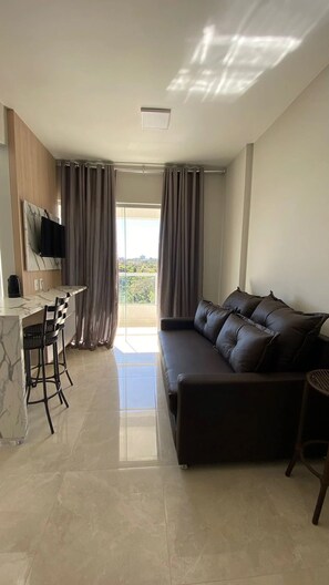 A modern living room with a sofa, a dining area with a table and chairs, and a TV mounted on the wall. - Caldas Novas - Recanto do Bosque Flat (Caldas Novas)