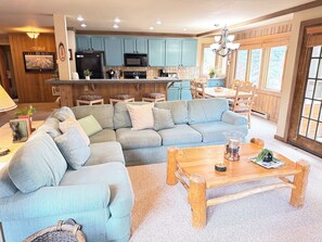 A living room with a sectional sofa, a wooden coffee table, and a kitchen area with blue cabinets and a microwave. - Spacious + Pet Friendly + Walk to Village - 2/2 (Mammoth Lakes)