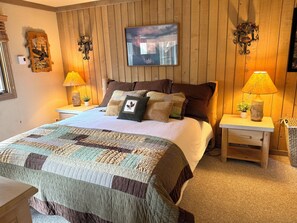 A bedroom with a wooden paneled wall, a bed with multiple pillows, two bedside lamps, and a framed picture above the bed. - Spacious + Pet Friendly + Walk to Village - 2/2 (Mammoth Lakes)