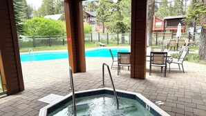 Een overdekt buitenzwembad met een jacuzzi, omringd door ligbedden en een houten terras.