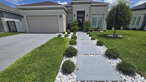 A residential driveway leading to a house with a garage, a front door, and a small tree. - Spacious, Comfortable Texas Stay for Extended Business & Family Visits. (Pharr)