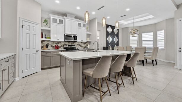 A modern kitchen with white cabinets, a central island, bar stools, pendant lighting, and a dining area with a table and chairs. - Spacious, Comfortable Texas Stay for Extended Business & Family Visits. (Pharr)