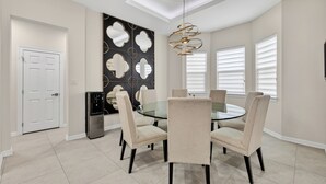 A dining area with a glass table, beige chairs, a black refrigerator, and a wall with a geometric mirror design. - Spacious, Comfortable Texas Stay for Extended Business & Family Visits. (Pharr)