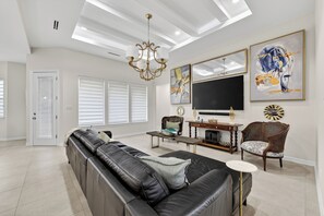 A spacious living room with a black leather sofa, a wooden coffee table, and a rattan chair. A large flat-screen TV is mounted on the wall, and there are two framed abstract paintings above it. - Spacious, Comfortable Texas Stay for Extended Business & Family Visits. (Pharr)