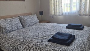 Ein Schlafzimmer mit einem Bett, einem Nachttisch mit Lampe, gemusterten Betttextilien, einem Bild an der Wand und einem Fenster mit Vorhängen.