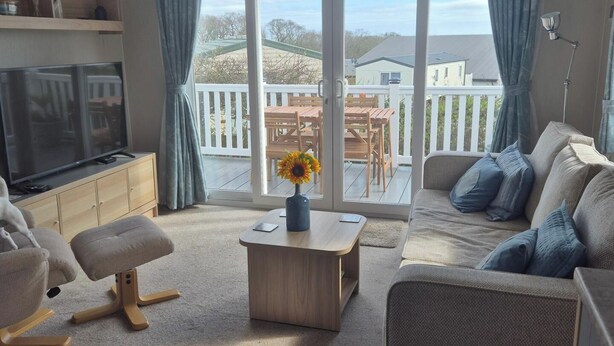 Ein Wohnzimmer mit Fernseher, Sofa, Couchtisch und Blick auf eine Terrasse und ein Haus.