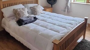 A bedroom with a wooden bed, a bedside table, a fan, and a window with curtains. - Irish Open 2026 - Sleeps 8 - 15 min from Doonbeg (Co Clare)