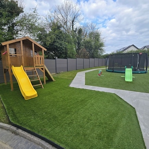 A backyard with a wooden playhouse, a yellow slide, a trampoline, and a green slide. - Irish Open 2026 - Sleeps 8 - 15 min from Doonbeg (Co Clare)