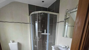 A bathroom with a glass-enclosed shower, a toilet, and a sink with cabinets. - Irish Open 2026 - Sleeps 8 - 15 min from Doonbeg (Co Clare)