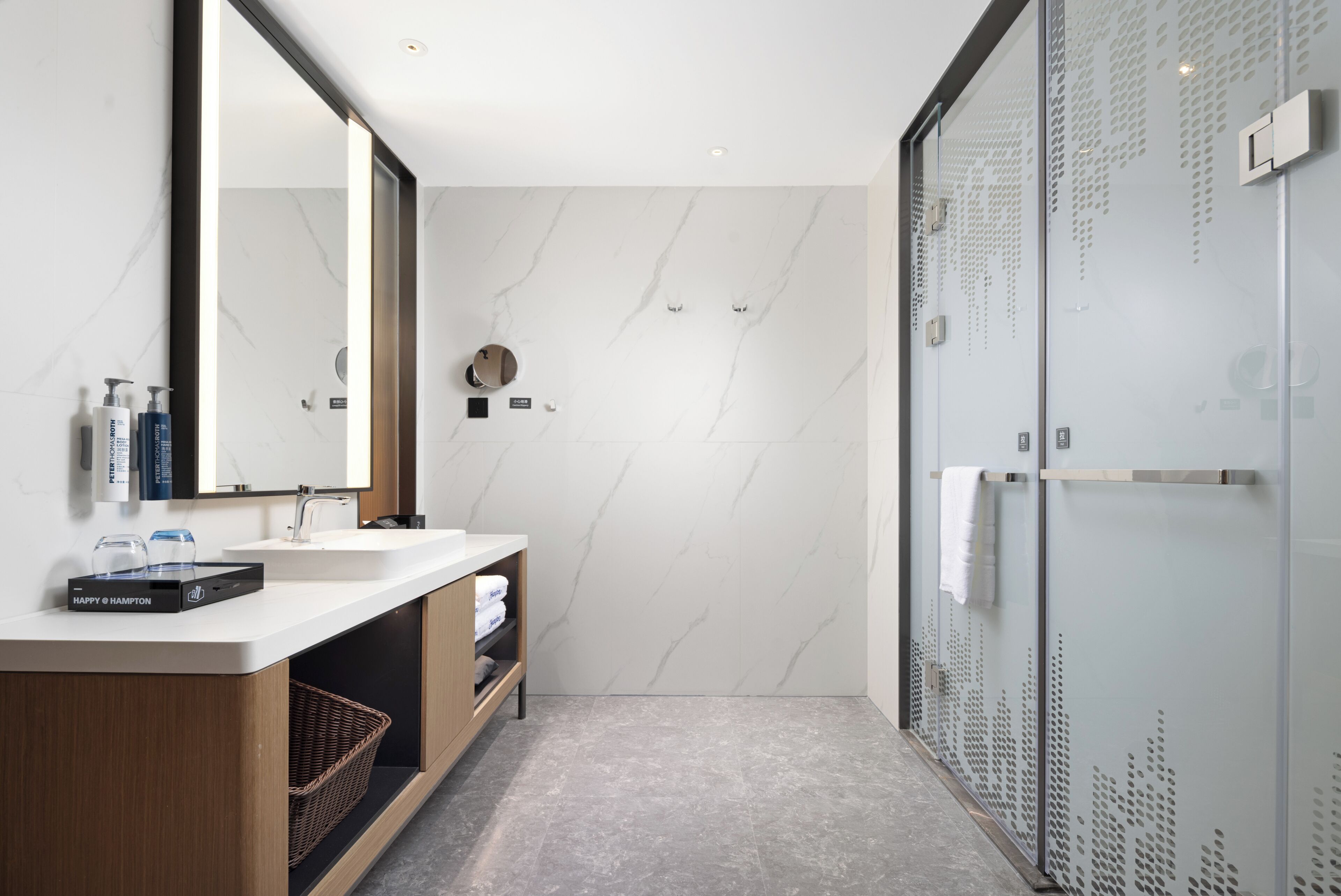 A modern bathroom with a marble wall, a large mirror, a sink, and a glass shower enclosure.