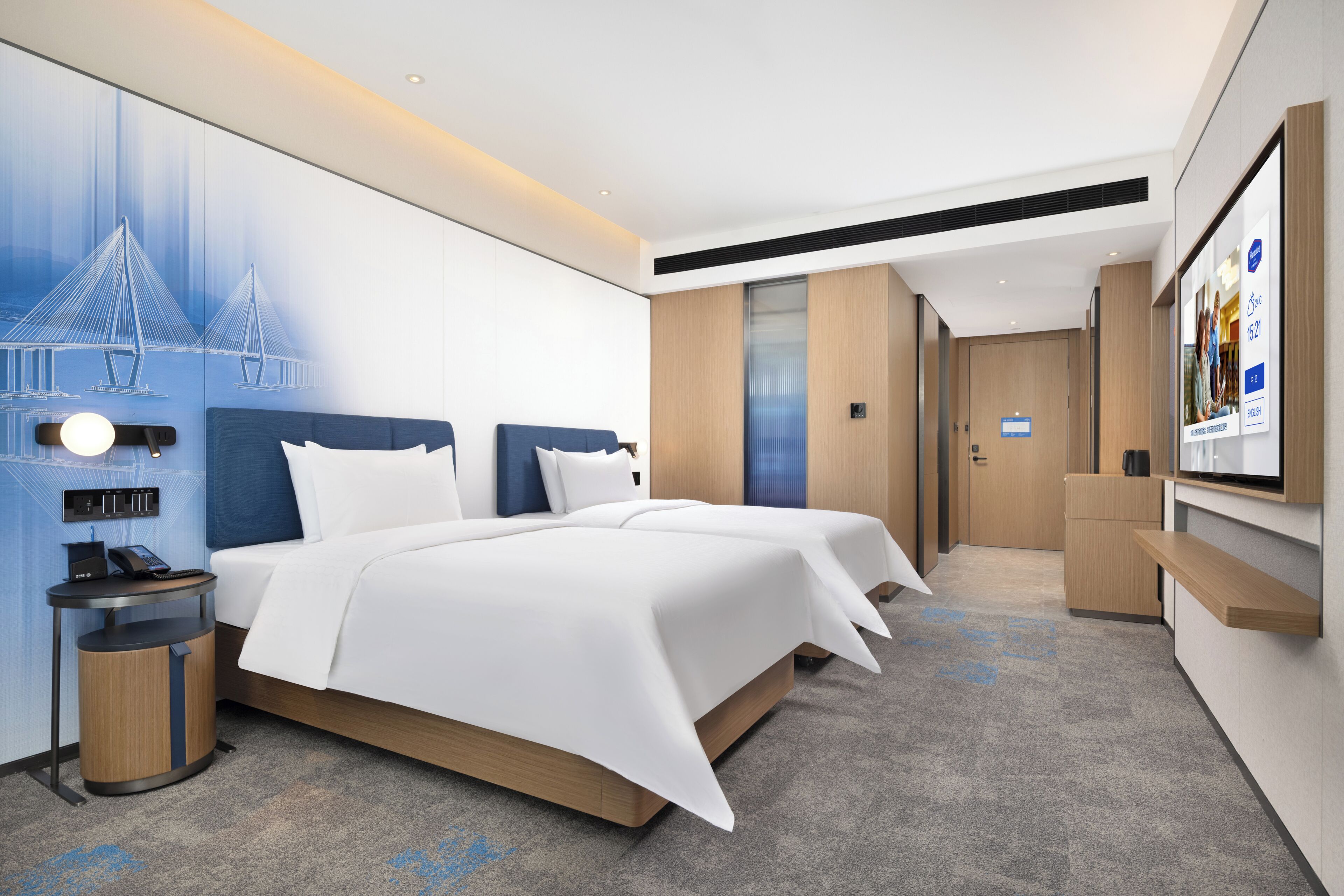 A modern hotel room with a large bed, a desk, a wall-mounted TV, and a cityscape mural.