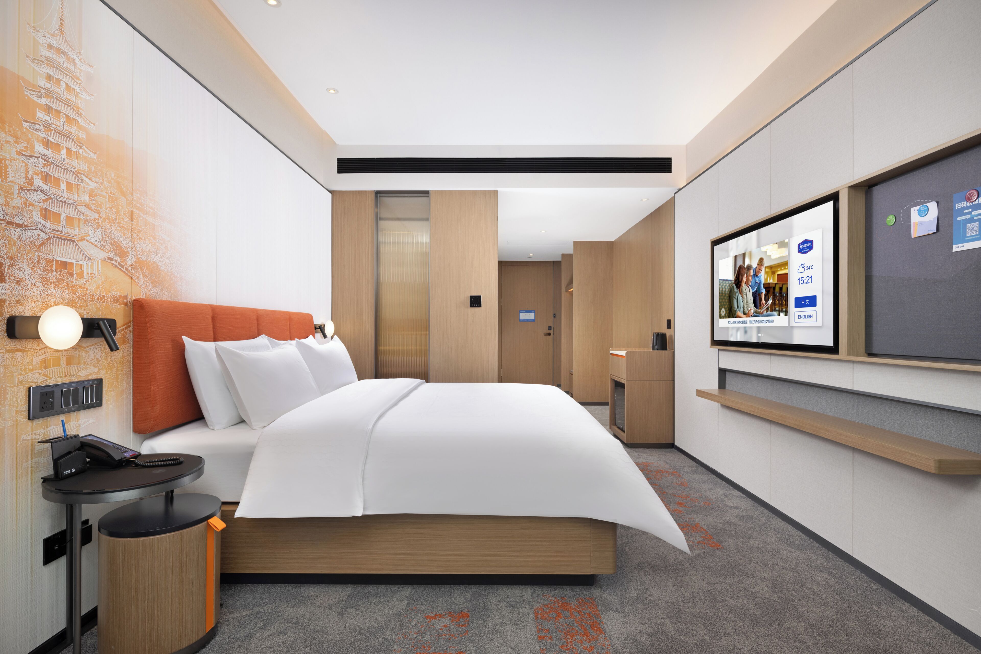 Habitación de hotel moderna con cama, escritorio con teléfono, televisor y estante en la pared.