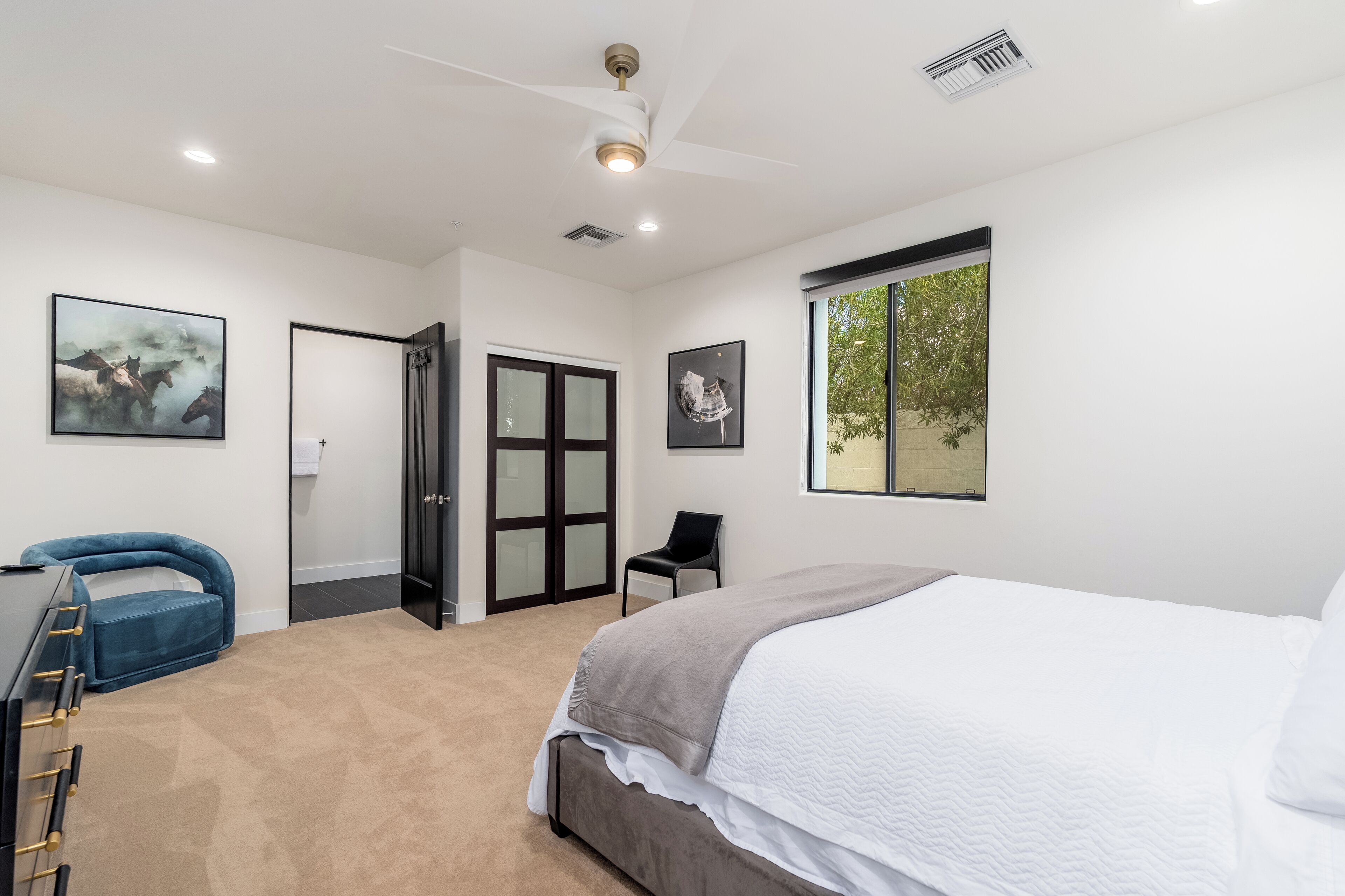 A bedroom with a bed, a desk, a chair, a ceiling fan, and a window.