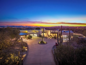 A modern building with a spacious driveway, surrounded by desert vegetation and cacti. - NEW SWSS 8BR Desert‑Modern Estate | Pool, Hot Tub, Golf Simulator, Cold Plunge, Putting Green (Scottsdale)
