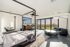 A modern bedroom with a large bed, a desk, and a view of the outdoors. - NEW SWSS 8BR Desert‑Modern Estate | Pool, Hot Tub, Golf Simulator, Cold Plunge, Putting Green (Scottsdale)