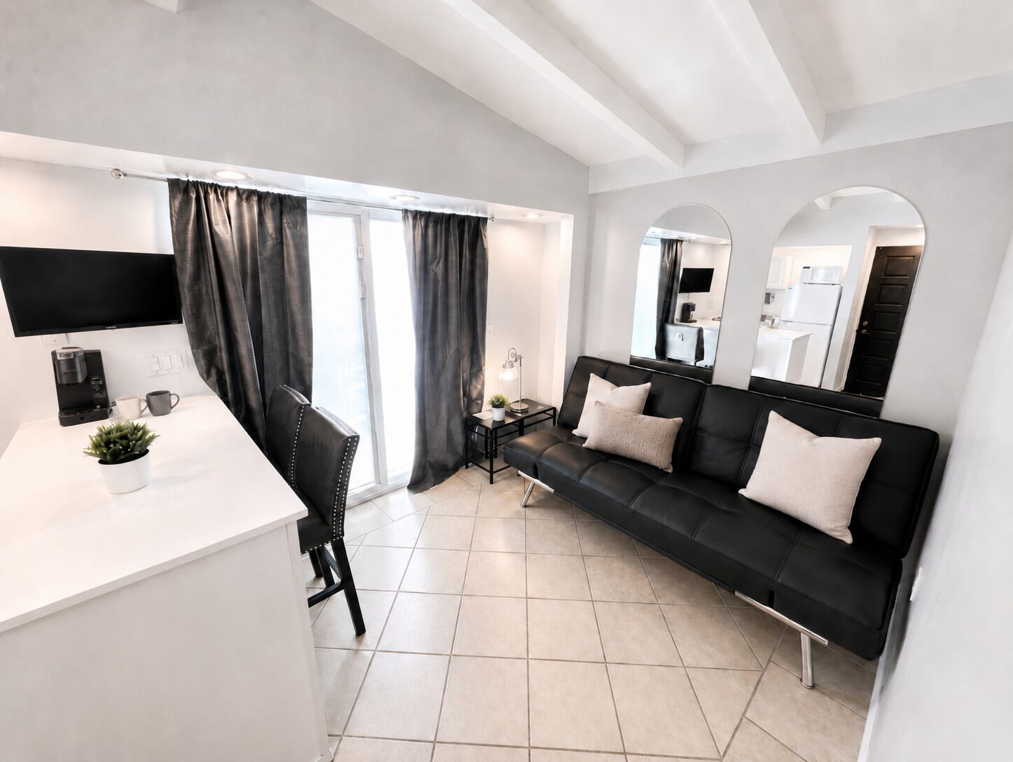 A modern living room with a black sofa, a white coffee table, a TV, and a large window with curtains.
