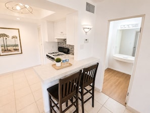 A modern kitchen with white cabinets, a gas stove, a small island with chairs, and a painting on the wall.