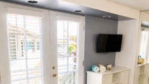 A living room with a sofa, a TV mounted on the wall, and a cabinet with decorative items. - Mykonos Desert Suites (Palm Springs)