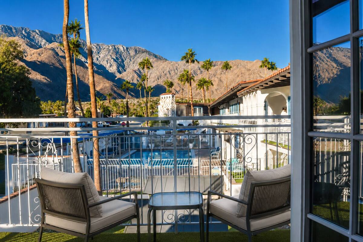 Un balcón con dos sillas y una mesa, con vista a una piscina y montañas.
