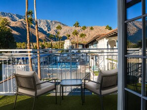 Un balcón con dos sillas y una mesa, con vista a una piscina y montañas.