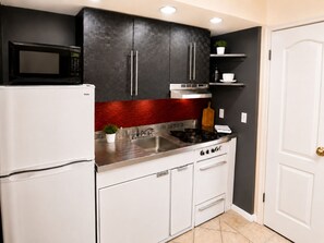 Una cocina compacta con microondas, estufa, fregadero y armarios blancos.