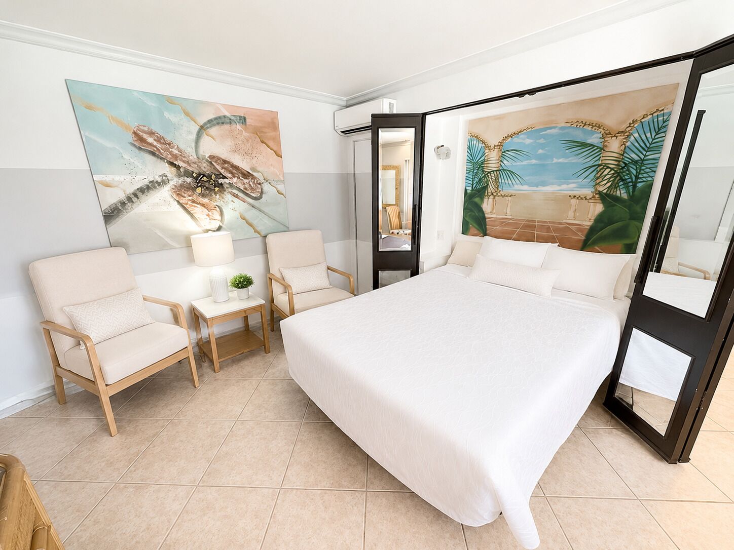Een hotelkamer met een bed, twee stoelen, een tafeltje en een schilderij aan de muur.