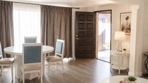 A hotel room with a dining area, a door leading outside, and a small table with a lamp and plant. - Mykonos Desert Suites (Palm Springs)