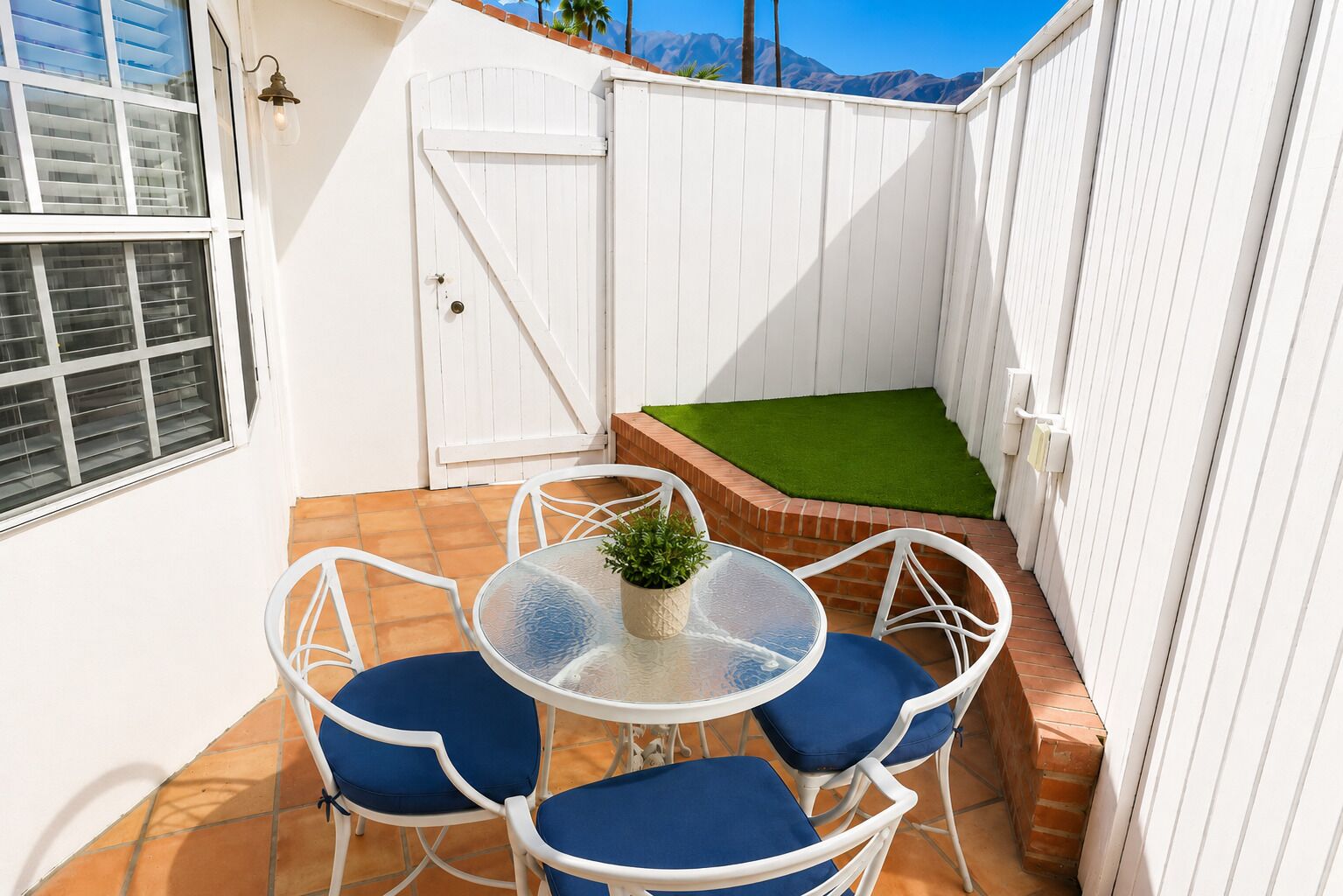 A patio with a table and chairs, a small green lawn, and a white fence.