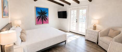 A bedroom with a bed, two nightstands, a chair, a television, and a door leading outside.