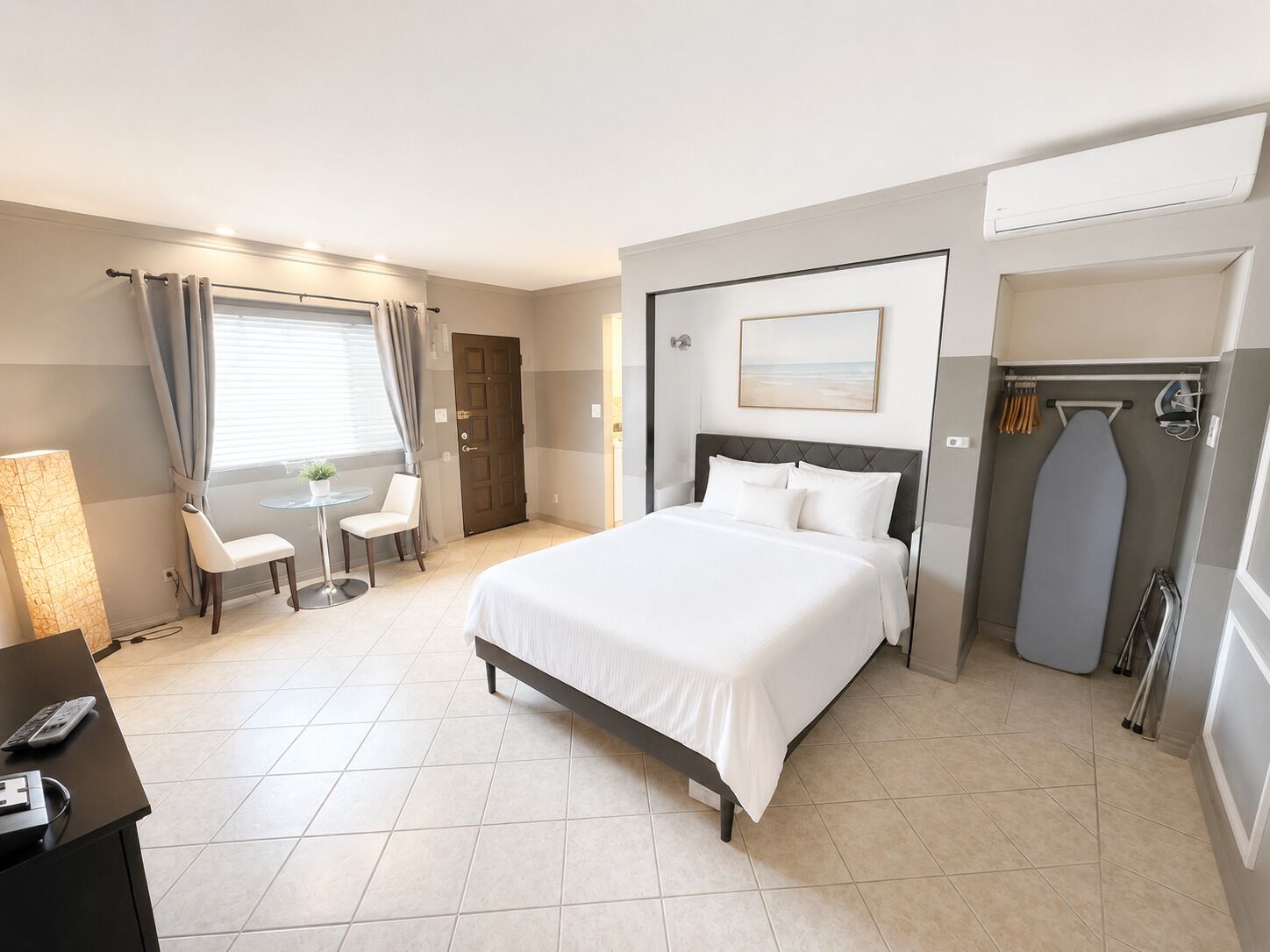 Una habitación de hotel con cama, escritorio con teléfono, silla, mesita con planta y ventana con cortinas.