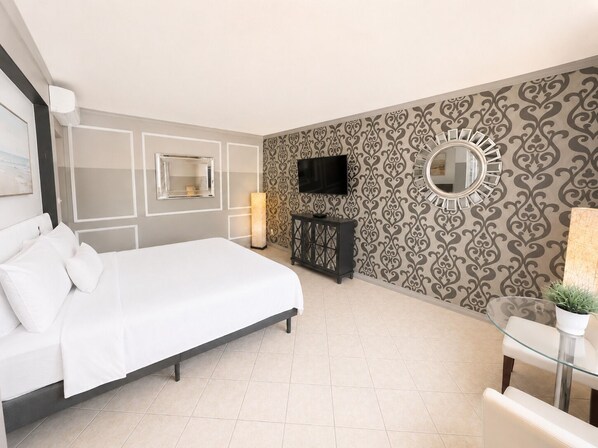 Habitación de hotel moderna con una cama, un televisor, un espejo y una pequeña mesa con una planta.