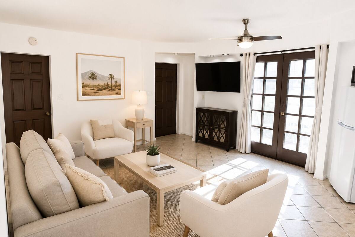 Una sala de estar con sofá, sillones, una mesa de centro, televisor y una puerta.