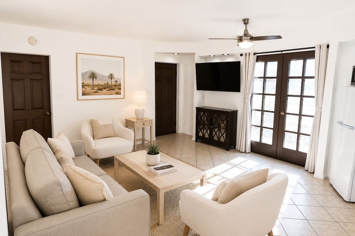 A living room with a sofa, armchairs, a coffee table, a TV, and a door.